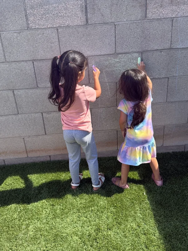 Two school-age girls drawing with chalk on the yard wall